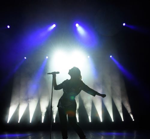 a woman in a black dress and a microphone in front of a stage with lights