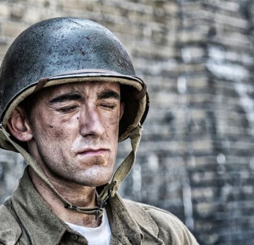 A weary WWII soldier with a dirt-smudged face wearing a steel combat helmet and uniform.