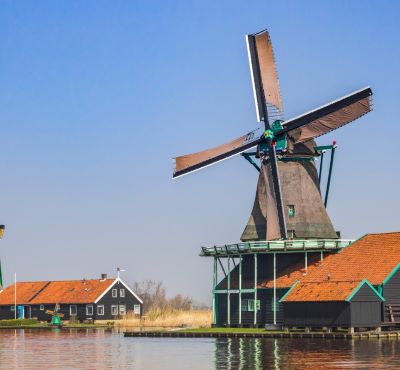 Historic Dutch windmill and wooden houses by the water at Zaanse Schans under a clear blue sky.