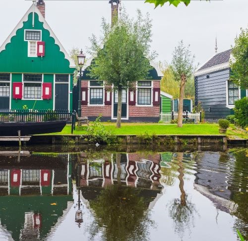 Traditional green Dutch houses with red shutters reflecting in a Zaanse Schans canal.