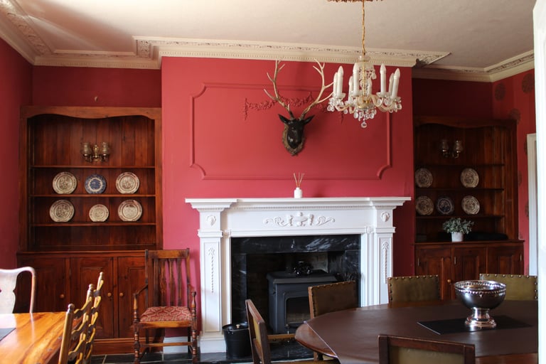 Elegant red dining room featuring a white mantel fireplace, deer head mount, and antique wooden hutches.