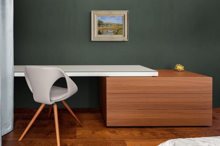 Modern home office featuring a white desk, wood drawers, and a grey swivel chair against a dark green wall.