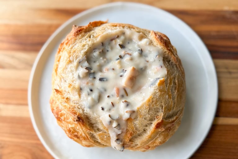 bread bowl on a wooden table with creamy chicken wild rice soup in it.