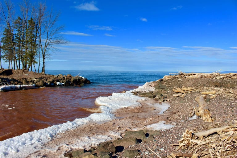 Snow-lined Lake Superior shoreline with blue water and scattered beach rocks