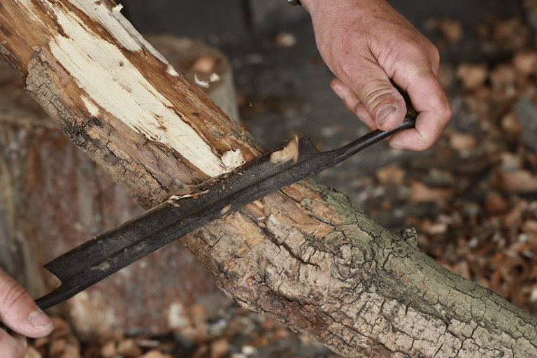 a person holding a drawknife and using it to remove bark