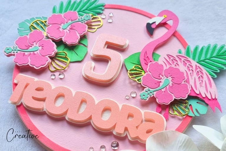 Cake topper with pink flamingo, flower and leaves. Number 5 and name Teodora are in the centre.