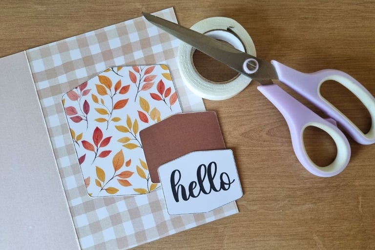 Greeting card materials on a wooden table, featuring autumn leaf patterns