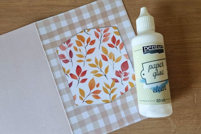An open greeting card with checkered beige and white patterns, featuring a cutout with autumn leaves