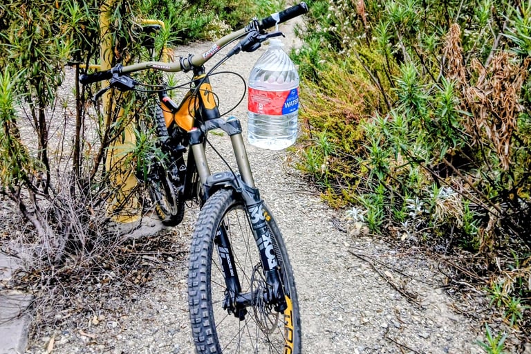 Mountain bike with Fox 36 fork leaning against trailside brush next to a distilled water jug used fo