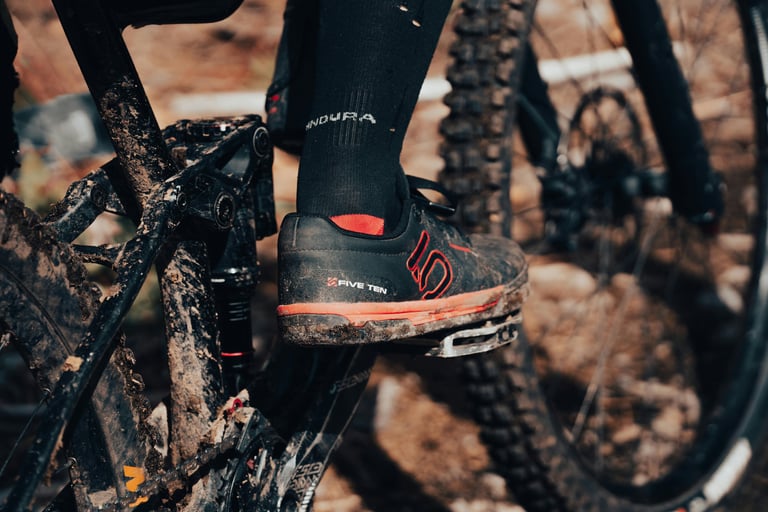 mountain biker wearing Five Ten shoes on flat pedals, covered in mud on a trail