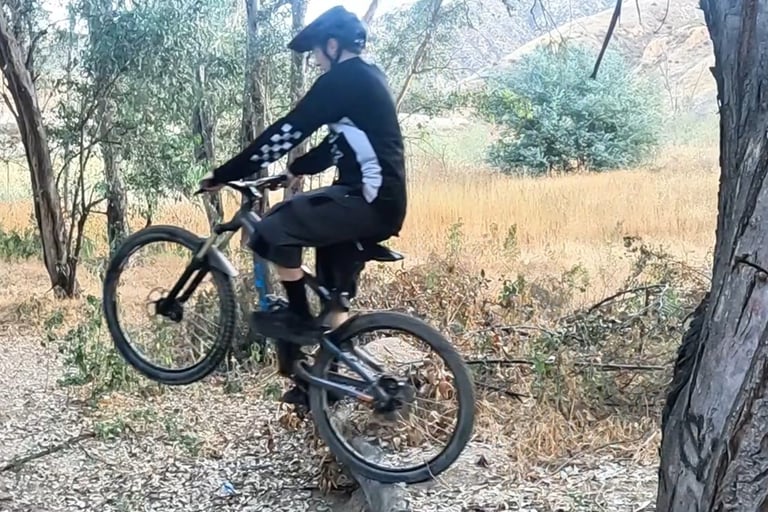 mountain biker in mid wheelie drop keeping finger on rear brake and body centered