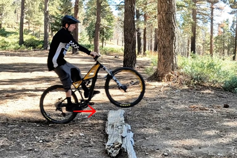 mountain biker pushing rear wheel into a log with feet to do the bump jump