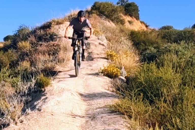 Mountain biker riding down a rocky singletrack trail in Southern California scrubland
