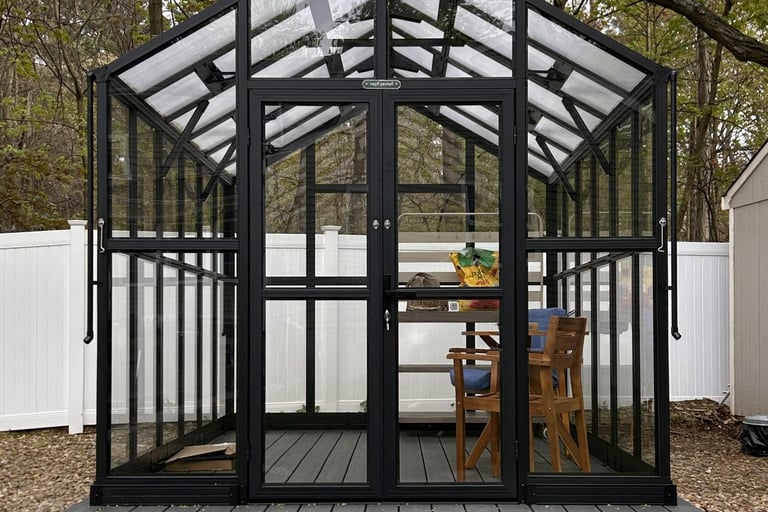 Front view of an assembled Vego Victorian greenhouse with black metal, glass side panels and polycarbonate roof panels.
