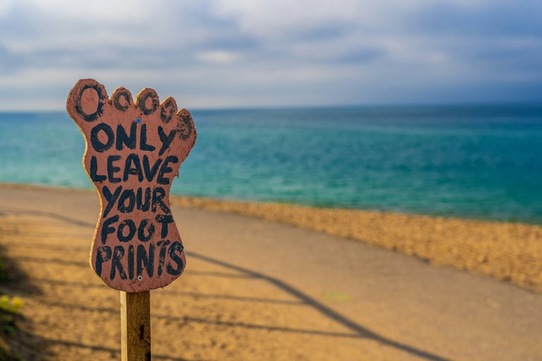 A foot shaped board 'only leave your foot prints written on it' in the backdrop of a sea.