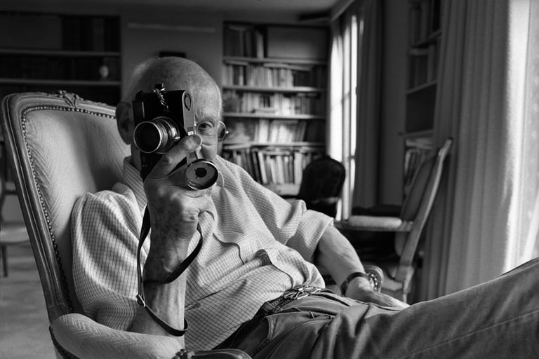 Henri Cartier-Bresson at home reclining in a chair with his faithful Leica in hand