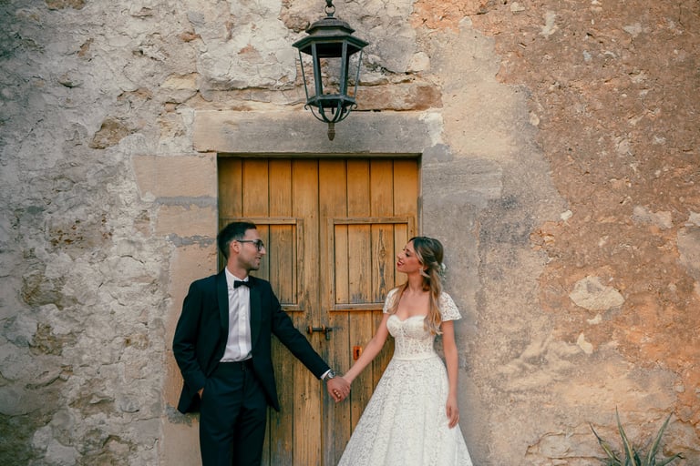  una sposa e uno sposo che si tengono per mano davanti un'antica porta siciliana