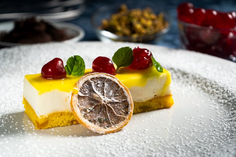 Due fette di torta gialla con crema bianca, glassa gialla, ciliegie rosse, menta e arancia essiccata