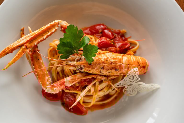 Tagliolini con scampi, pomodorini e prezzemolo in piatto bianco, guarnite con decorazione