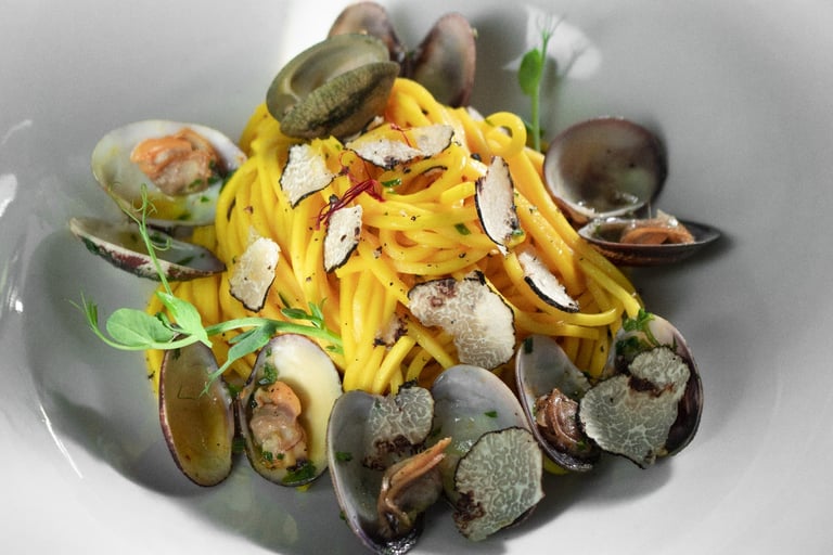 Spaghetti con vongole e tartufo in piatto bianco, con conchiglie aperte e germogli verdi