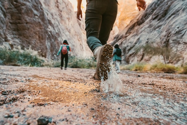 3 people walking through a canyon, boots stomping in the mud