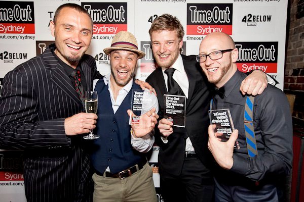 a group of men standing around celebrating winning 3 awards at an event