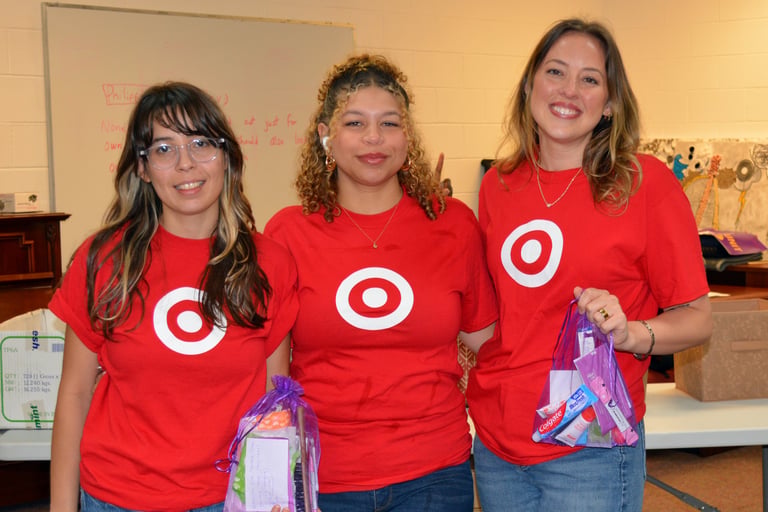 three women in red shirts are standing in a room holding hygiene kits