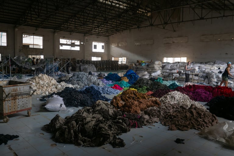 Multiple large color-coded piles of fabric in a warehouse