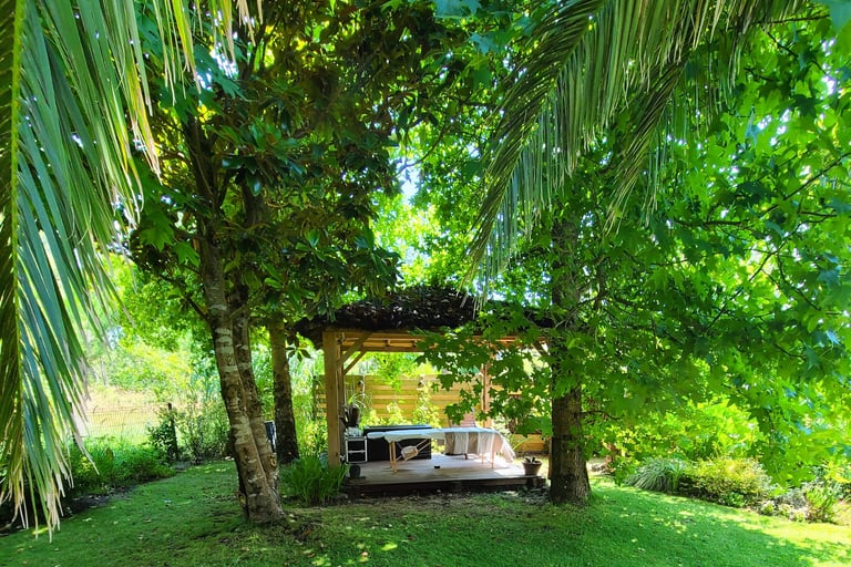 Table de massage installée sous un gazebo balinais en bois au mileu d'un jardin luxuriant