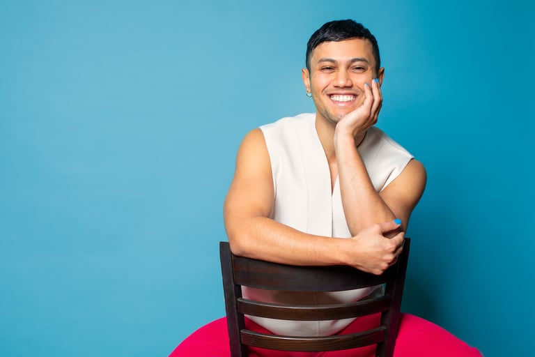 Founder sitting on a reversed brown chair. They are smiling and wearing a short-sleeve offwhite top.