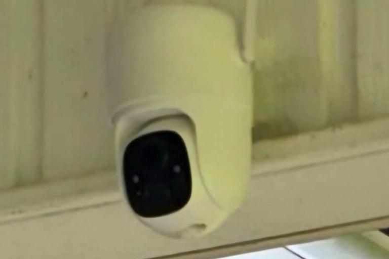 A white outdoor smart security camera with dual antennas mounted under a roof for home surveillance.