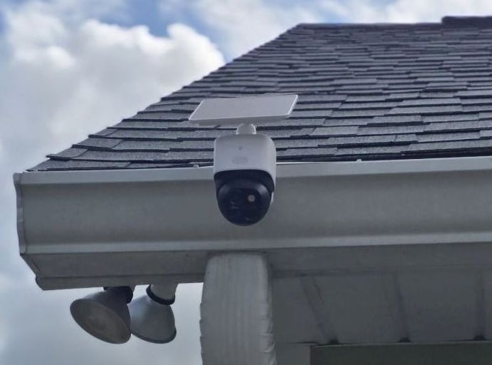 White solar-powered wireless outdoor security camera mounted on a residential roof gutter system.