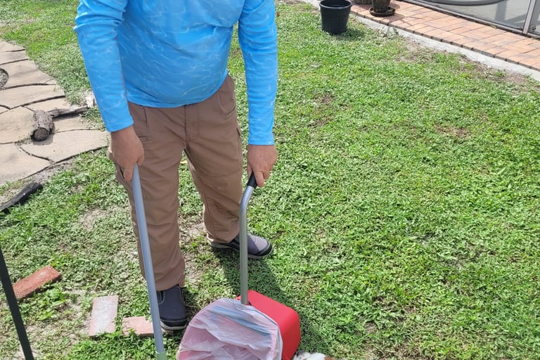 Robert using a sanitized scooper to remove waste from a customers back yard, small dog watching him