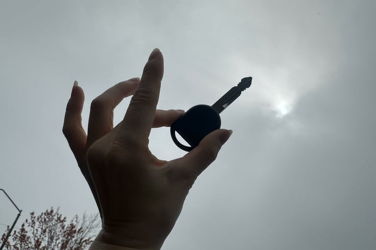 Hand holding a car key silhouette against an overcast sky