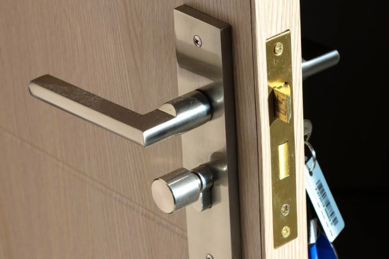 Close-up of a wooden residential door showing both inside/outside handles, with a key in the keyhole & a secure lock
