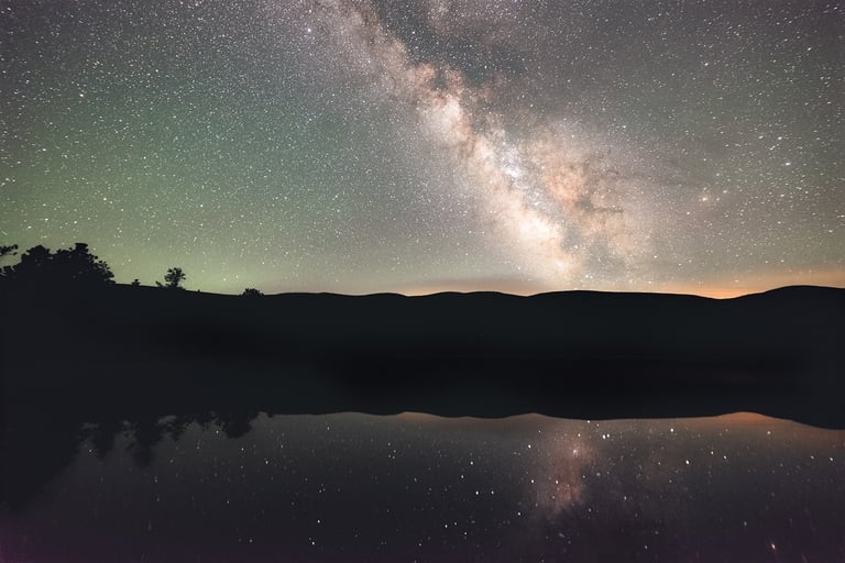 Vibrant Milky Way galaxy reflecting in a calm lake with mountain silhouettes under a starry night sky.
