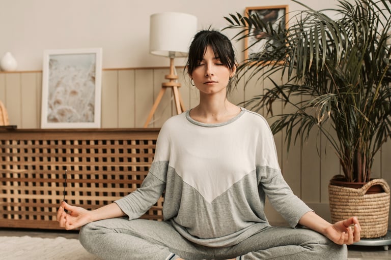 A woman practicing mindful meditation in a lotus pose during a home yoga session.