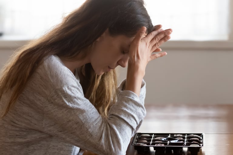 Stressed woman struggling with emotional eating while looking at a box of chocolates.