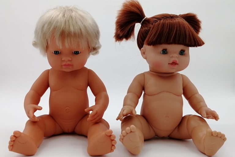 A Miniland doll sitting next to a Minikane doll