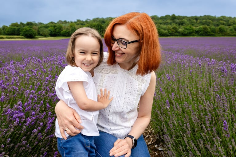 A smiling mother and daughter hugging in a vibrant purple lavender field during summer.