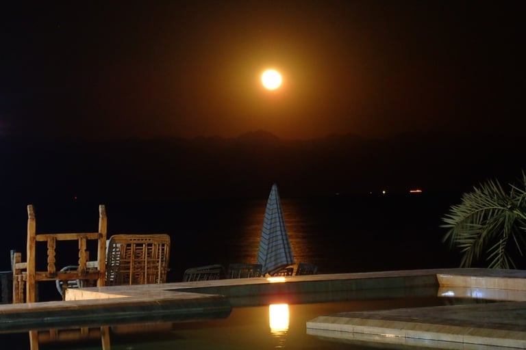 a full moon in the sky reflecting in the swimming pool in front of the sea