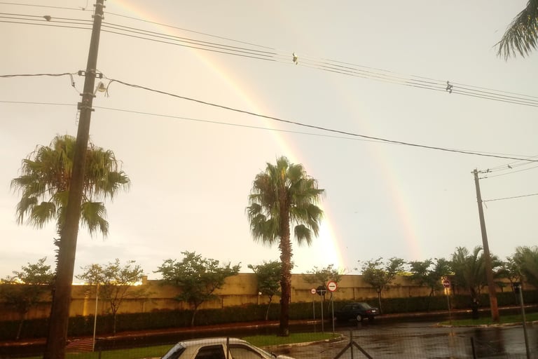 a rainbow - colored rainbow over a car parked in front of a fenced in