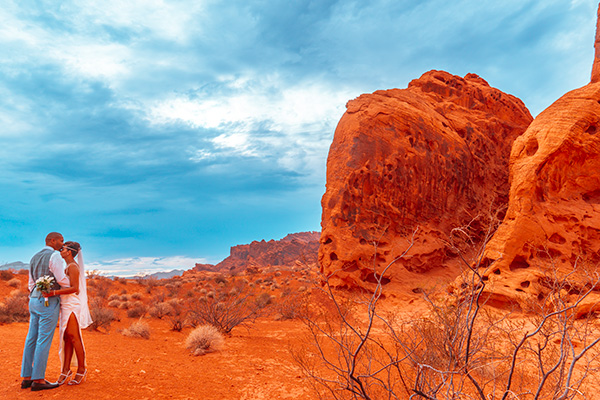 A newlywed couple embraces at a Valley of Fire desert wedding among red rock formations.