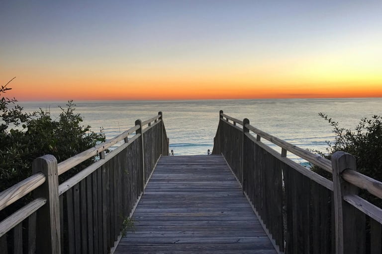 a wooden walkway leading to the beach at sunset