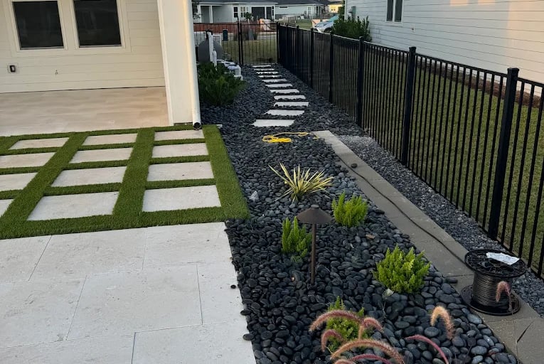 a backyard patio with a gravel path and a black iron fence