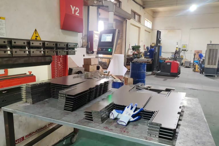 Precision sheet metal fabrication workshop featuring a CNC bending machine and stacked steel parts.