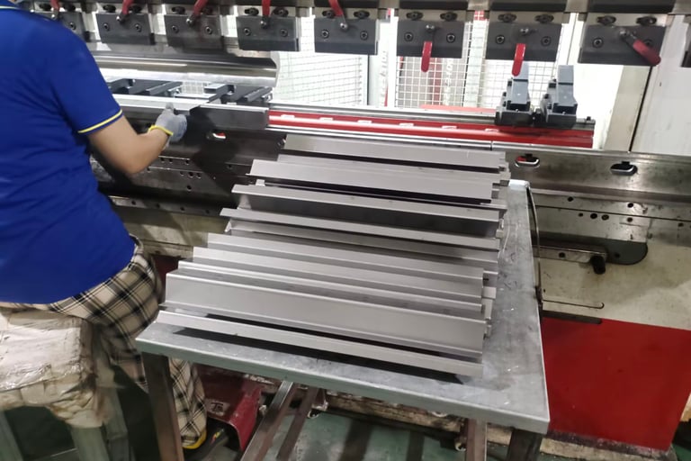 A factory worker operating a metal hydraulic press brake machine to bend steel sheets.