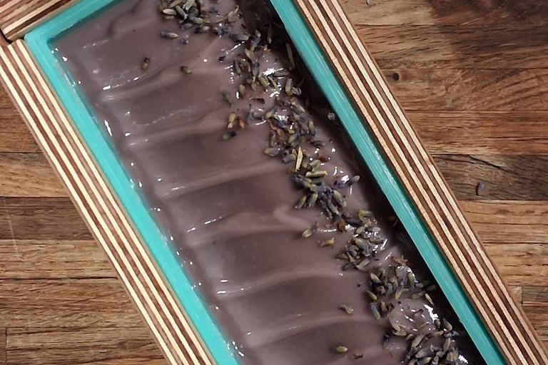 Handmade purple lavender soap curing in a wooden loaf mold with dried botanical toppings.