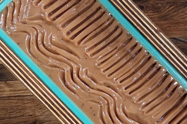 Freshly poured artisan soap batter with textured wavy patterns in a blue lined loaf mold.