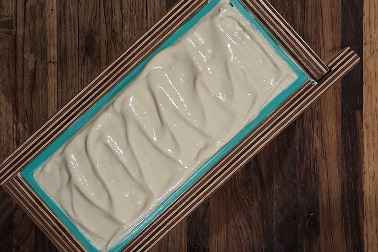 Handmade soap batter with textured peaks in a wooden loaf mold with a teal silicone liner.
